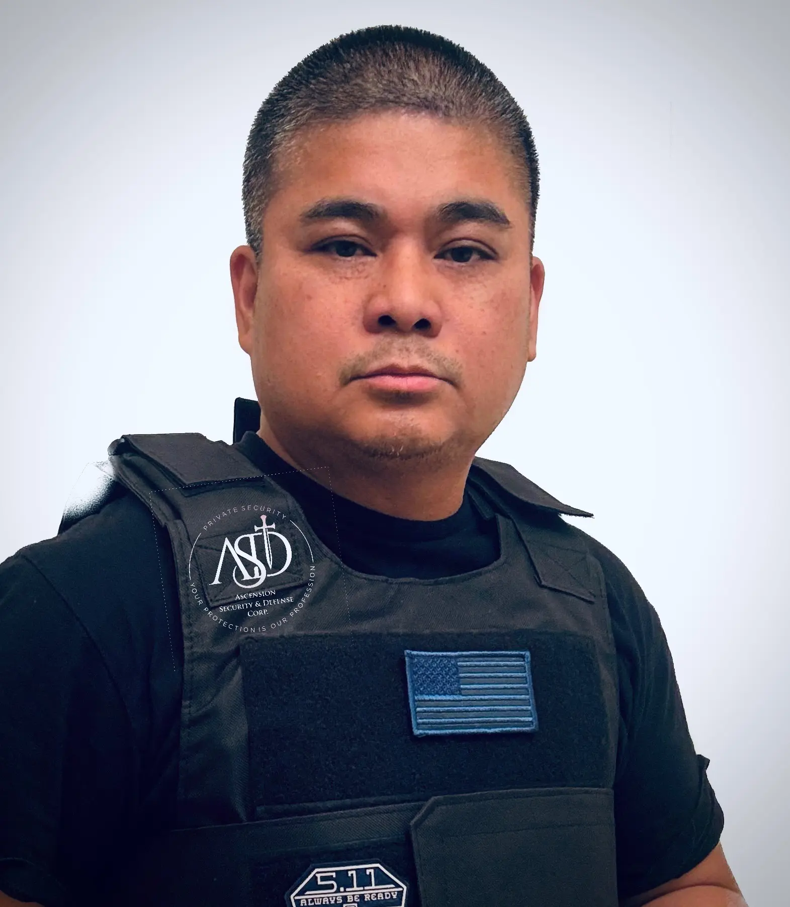 Man wearing black tactical vest, neutral expression.